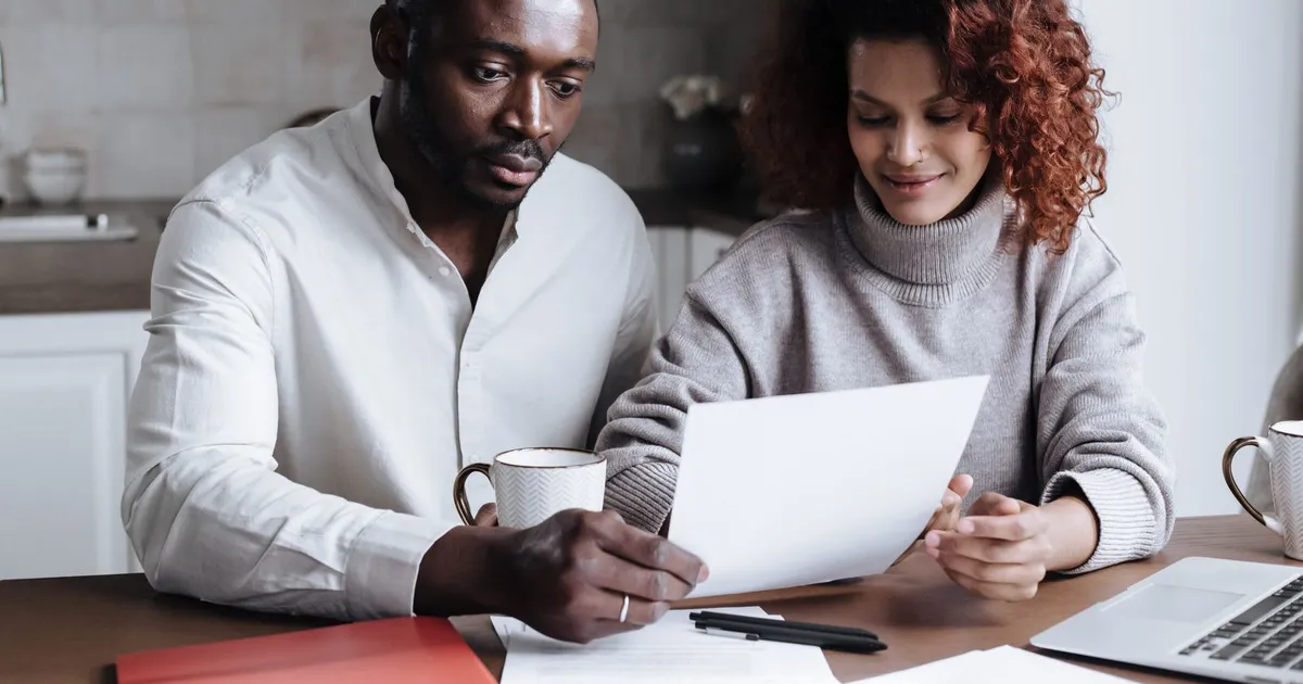Couple at a kitchen table reading the paperwork for a consumer proposal, weighing the consumer proposal disadvantages before signing