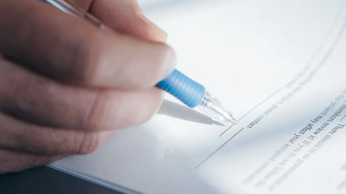 Close-up of a hand with a blue pen signing a document, the final step when you write a cheque